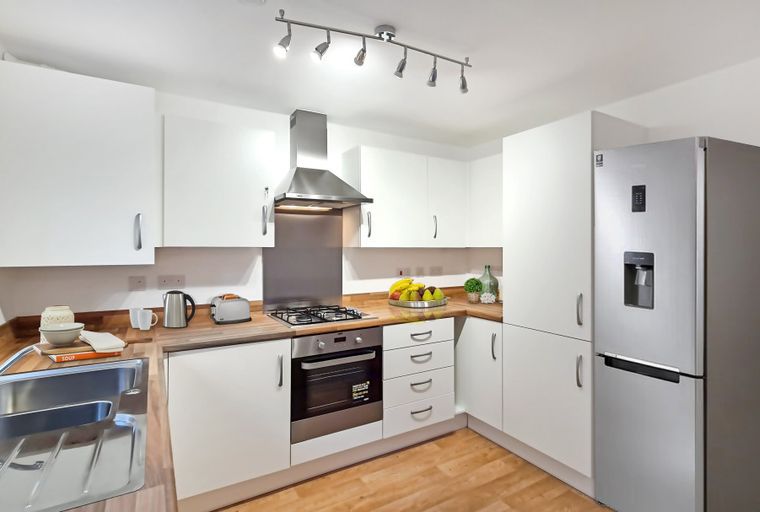 A modern kitchen with white cabinets, a stainless steel sink, a gas stove, and a refrigerator.