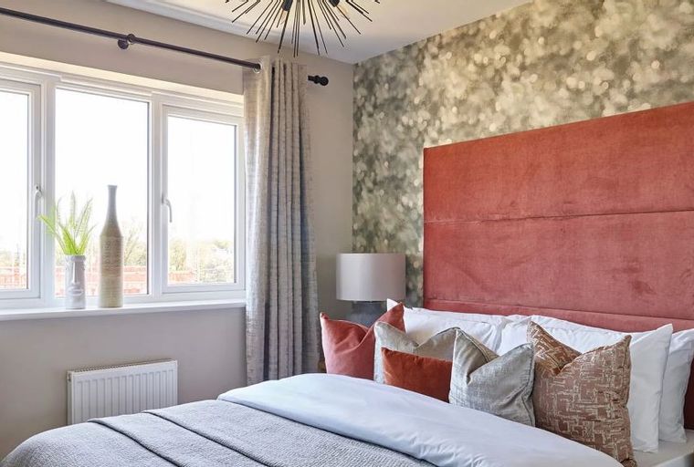 A bedroom with a large window, a bed with a coral headboard, and decorative pillows.