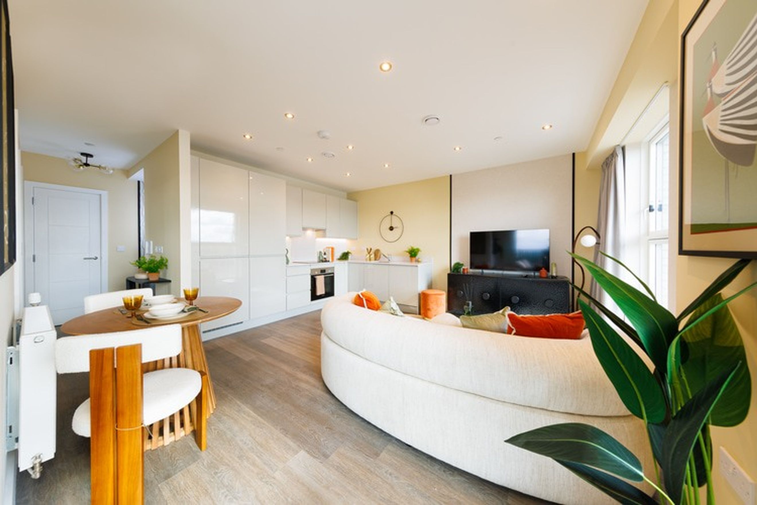 A living room and kitchen area with a curved sofa, dining table, and modern kitchen cabinets.