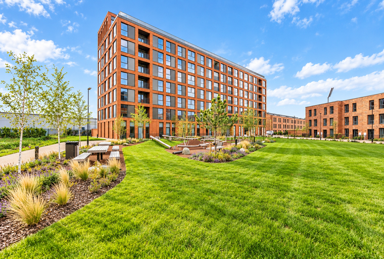 A modern apartment complex with brick buildings and a large green lawn.