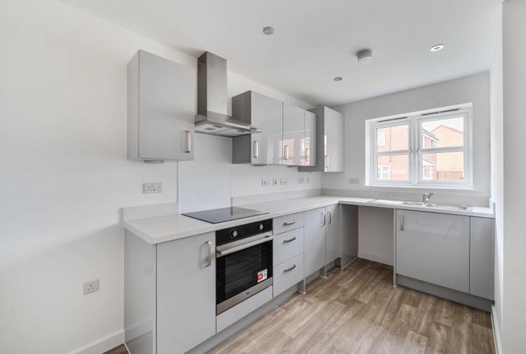 A modern kitchen with grey cabinets, a built-in oven, and a sink under a window.