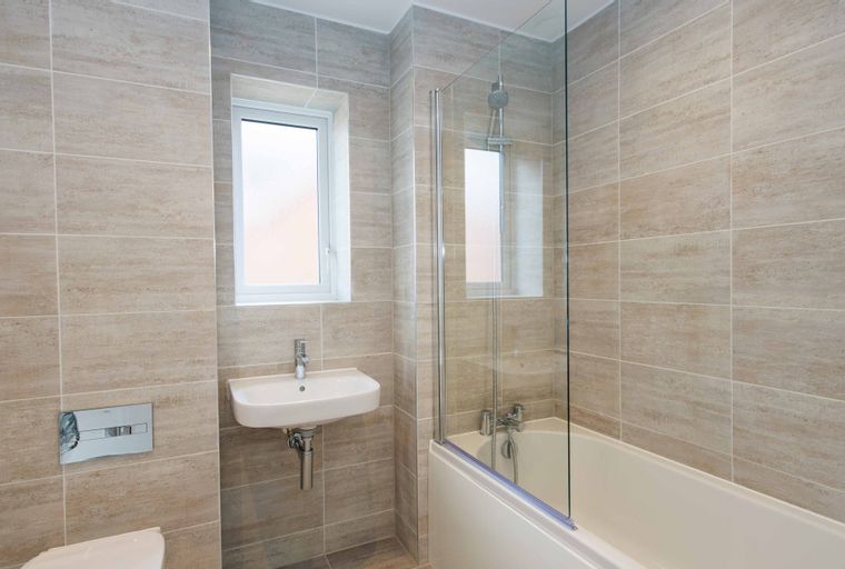 A bathroom with a sink, toilet, and bathtub with a shower screen.