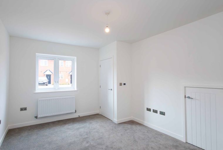 A bedroom with a window, two doors, and a radiator.