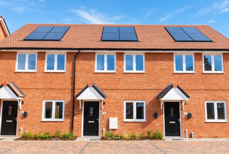 A row of modern brick townhouses with solar panels on the roof and black front doors.