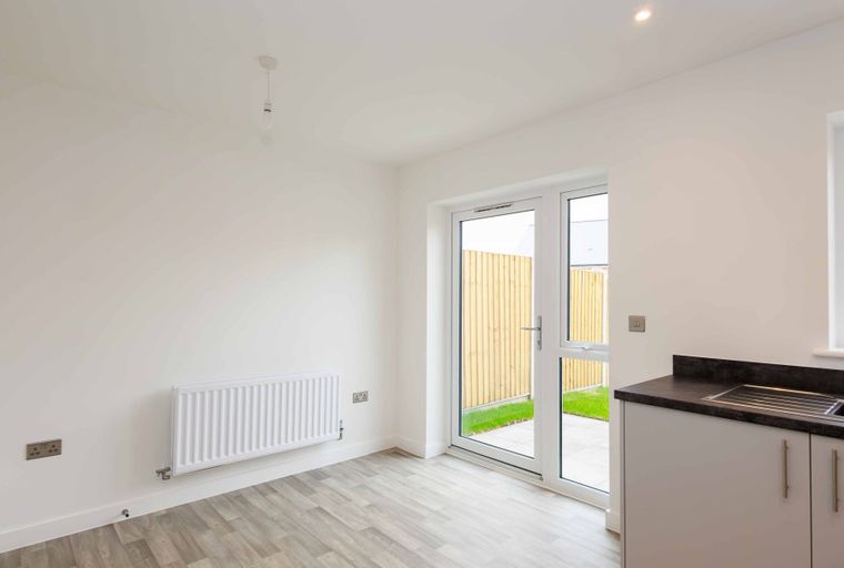 A room with a kitchen counter, sink, radiator, and French doors leading to a garden.