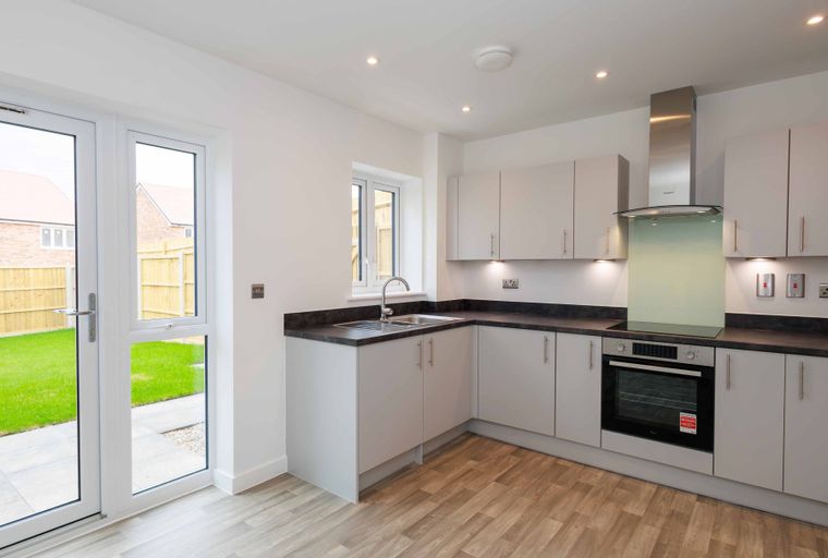 A modern kitchen with light gray cabinets, a dark countertop, a sink, and an oven, with double doors leading to a garden.