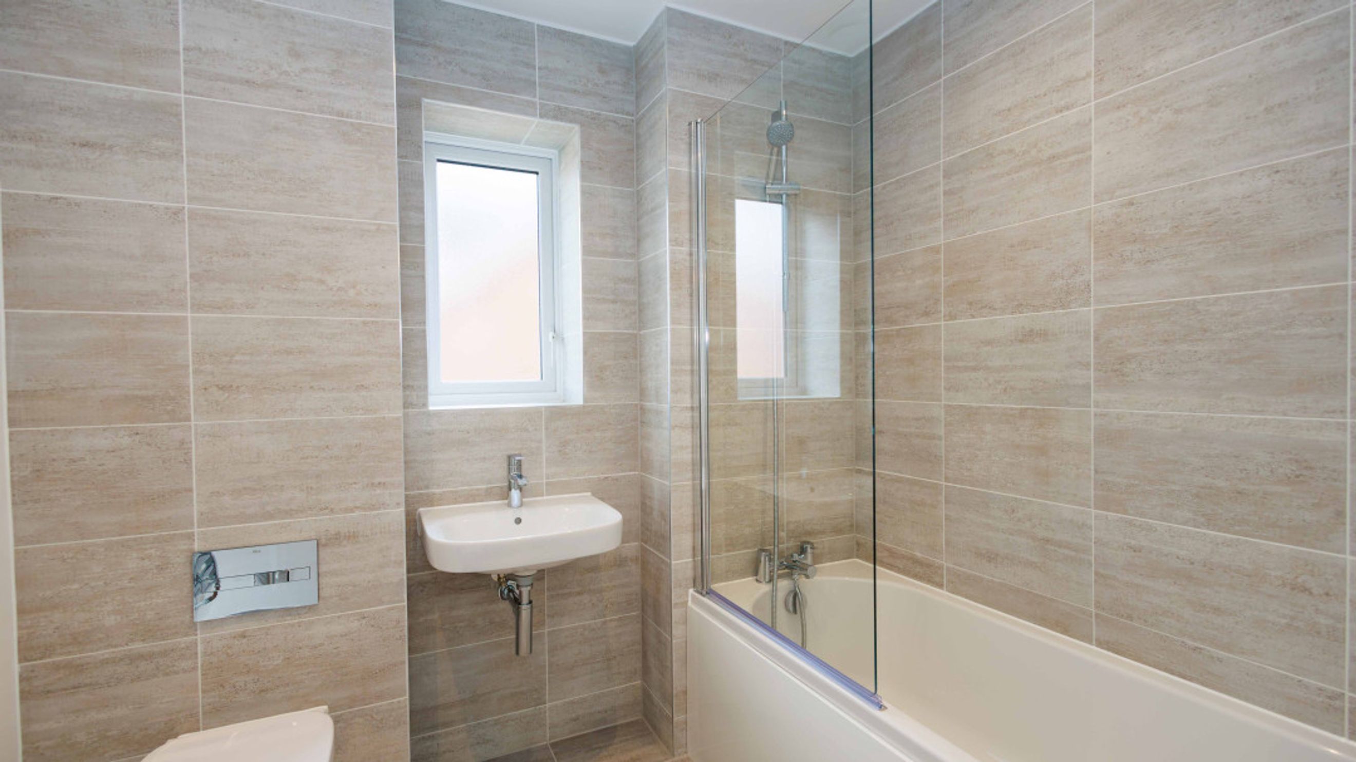 A bathroom with a sink, toilet, and bathtub with a shower screen.
