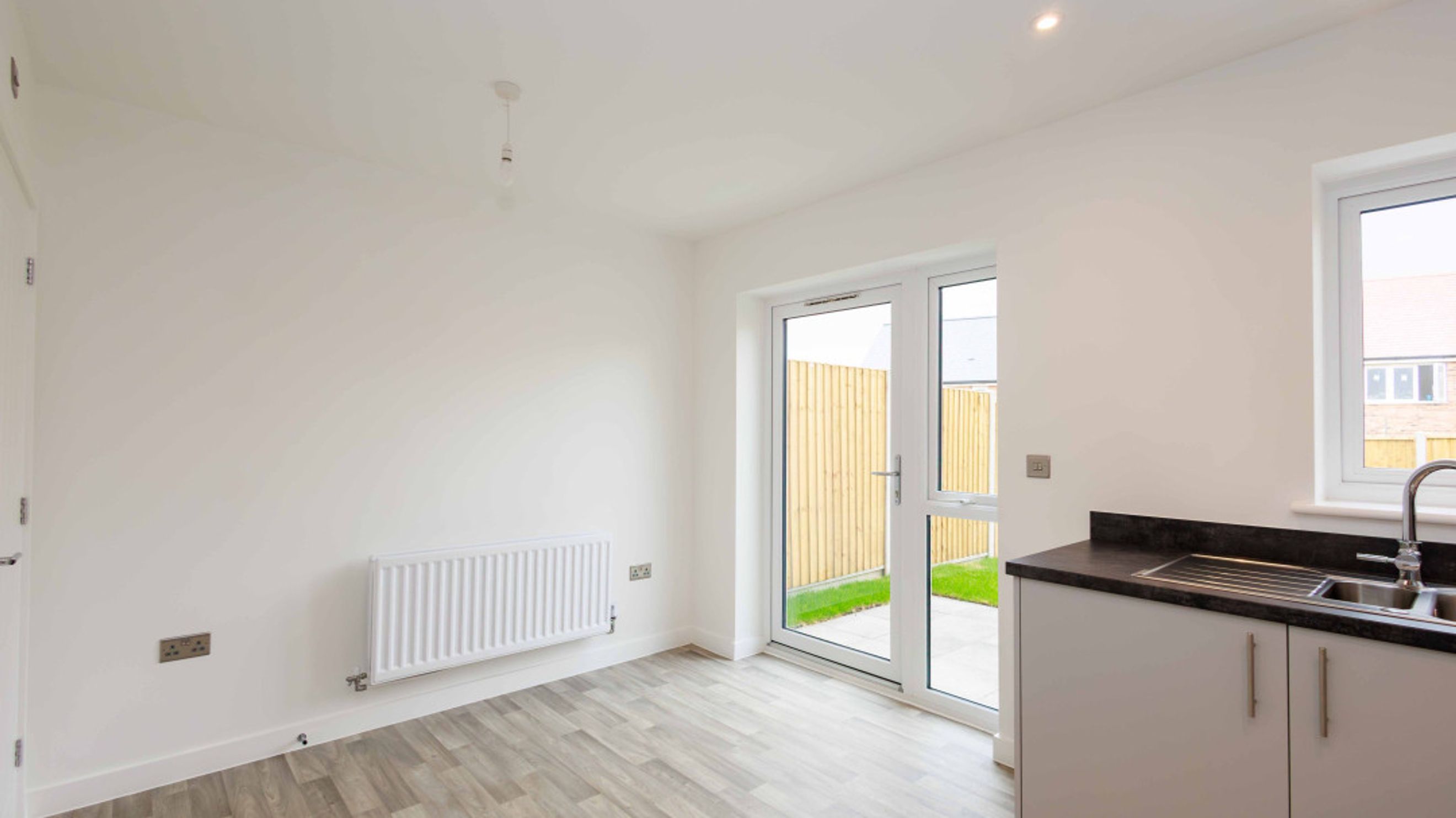 A room with a kitchen counter, sink, radiator, and French doors leading to a garden.