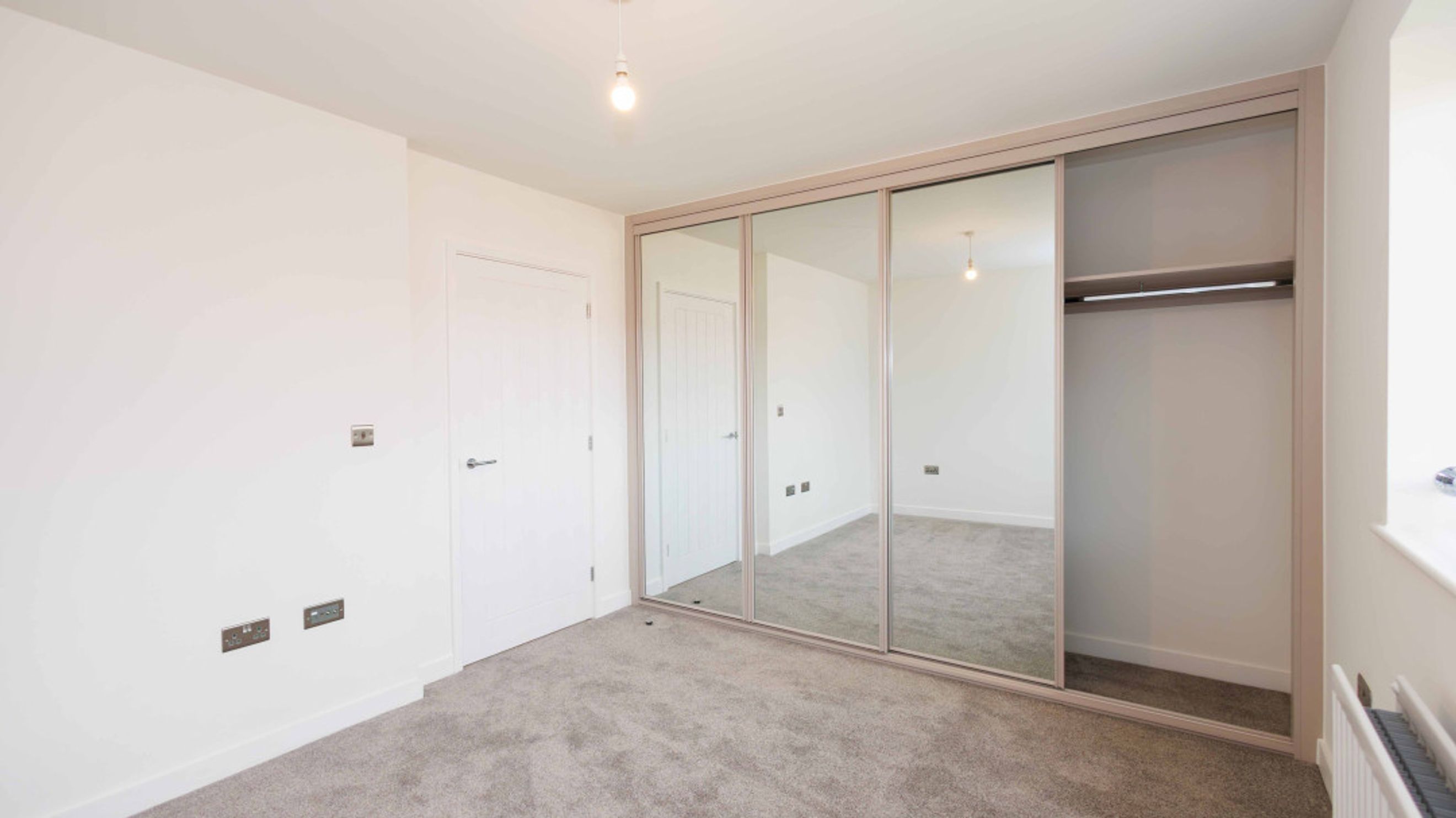 A bedroom with a large mirrored wardrobe and a white door.