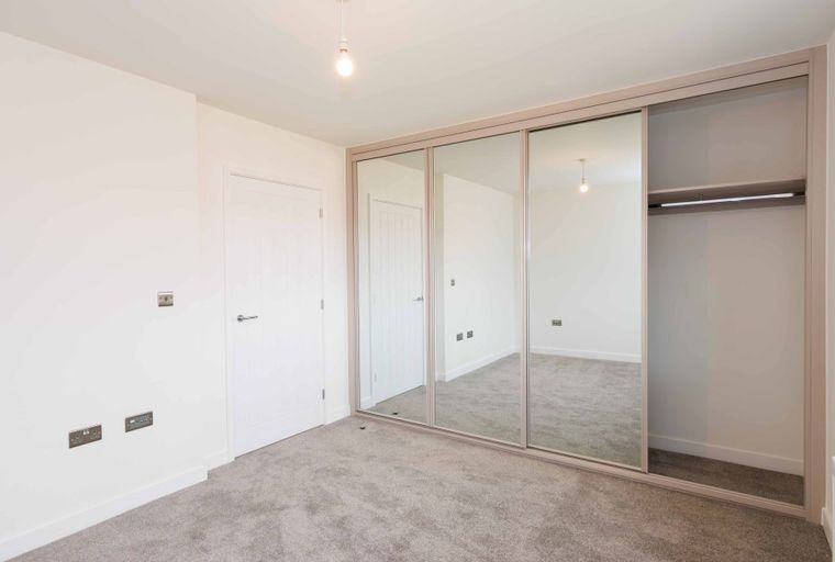 A bedroom with a large mirrored wardrobe and a white door.
