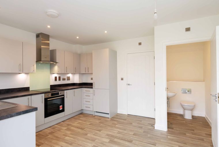 A kitchen and bathroom area with cabinets, a sink, a toilet, and an oven.