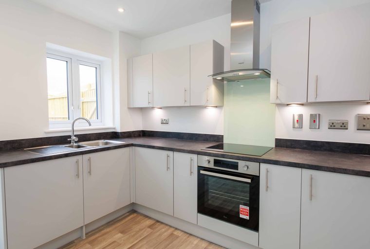 A modern kitchen with light gray cabinets, a dark countertop, a sink, an oven, and an extractor hood.