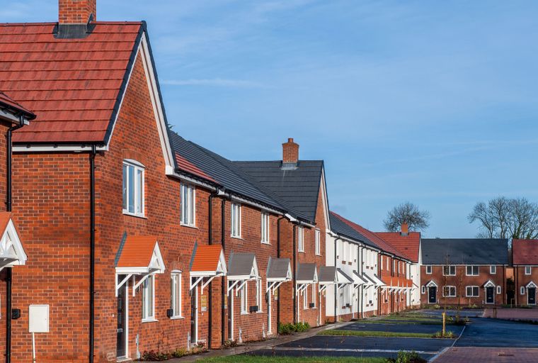 A row of new brick houses with red tile roofs under a blue sky.