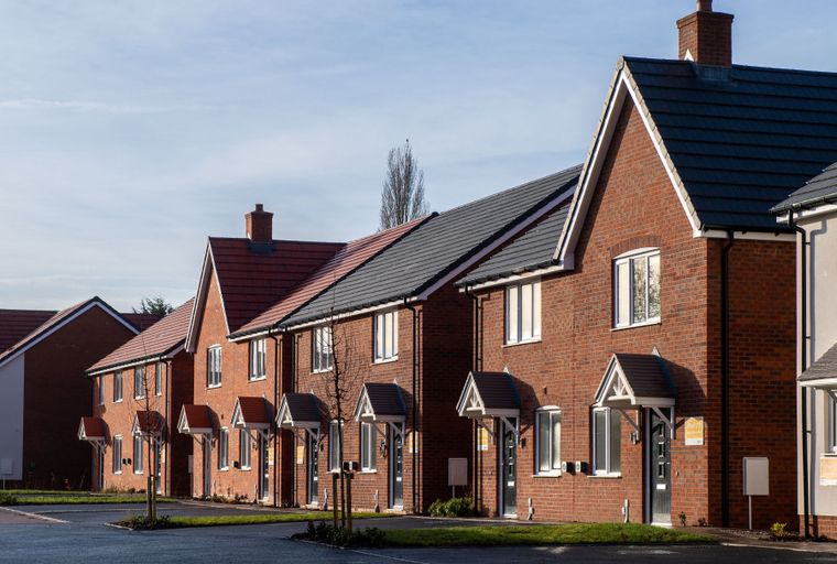 A row of newly built brick houses with tiled roofs and front porches.