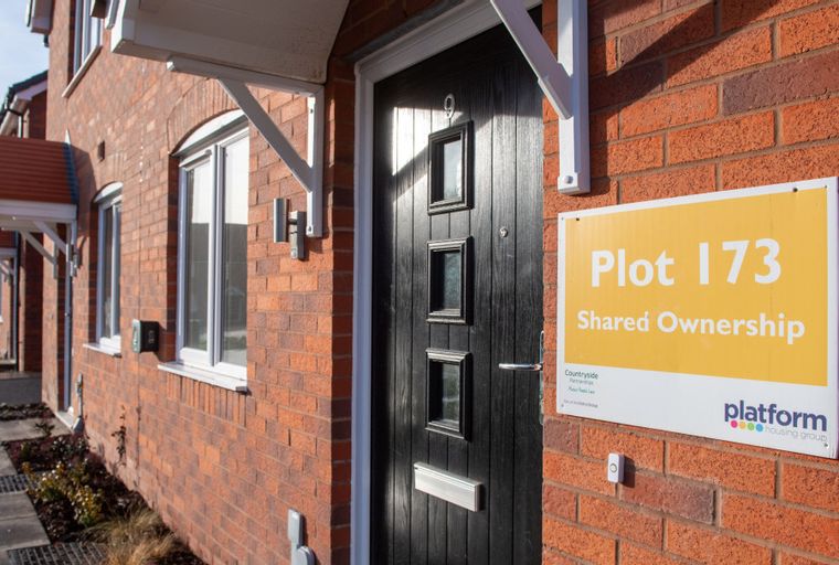 A brick house with a black front door and a yellow sign that says 'Plot 173 Shared Ownership'.