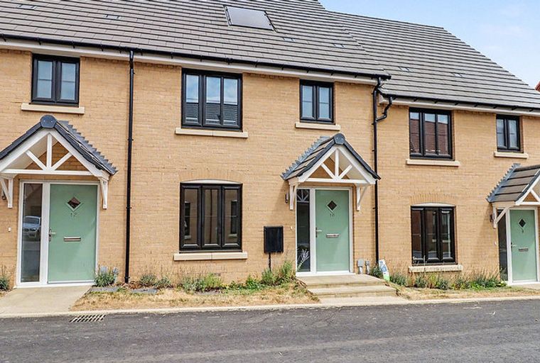 A row of modern townhouses with light brick exteriors and green front doors.