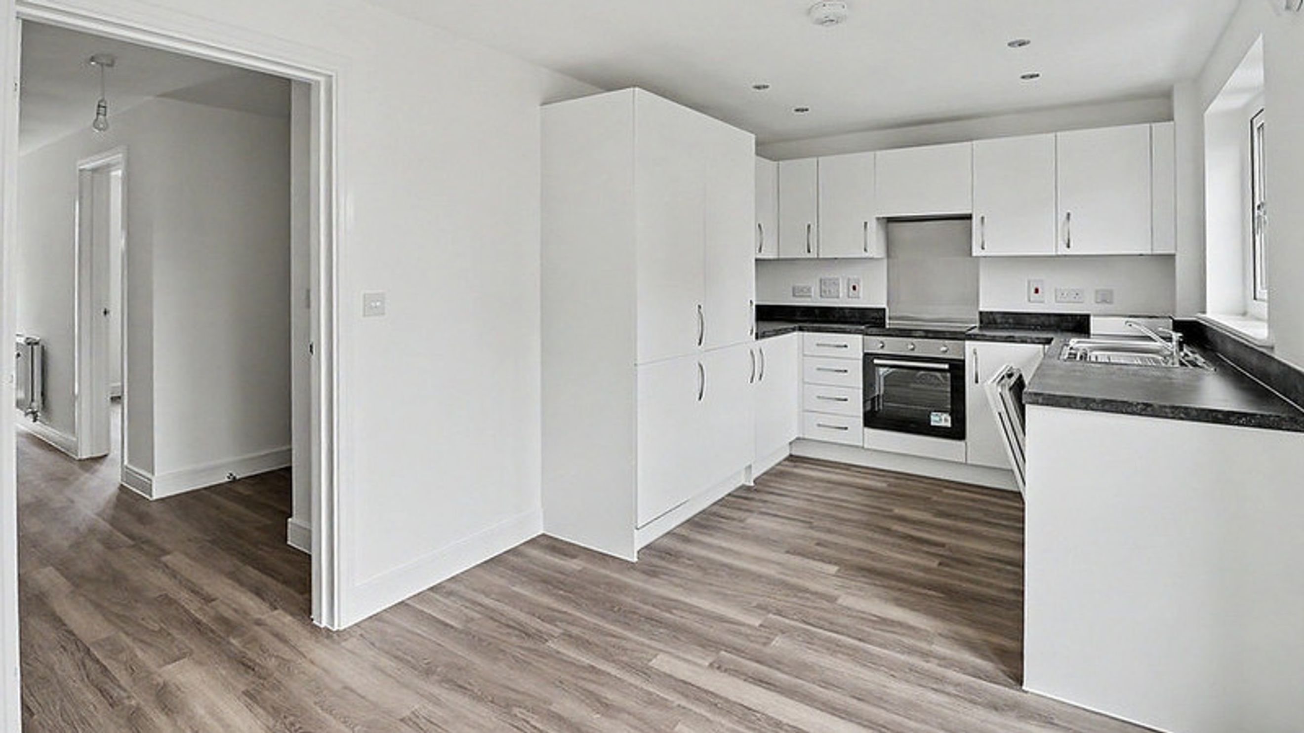 A modern kitchen with white cabinets, a dark countertop, and a built-in oven, adjacent to a hallway.