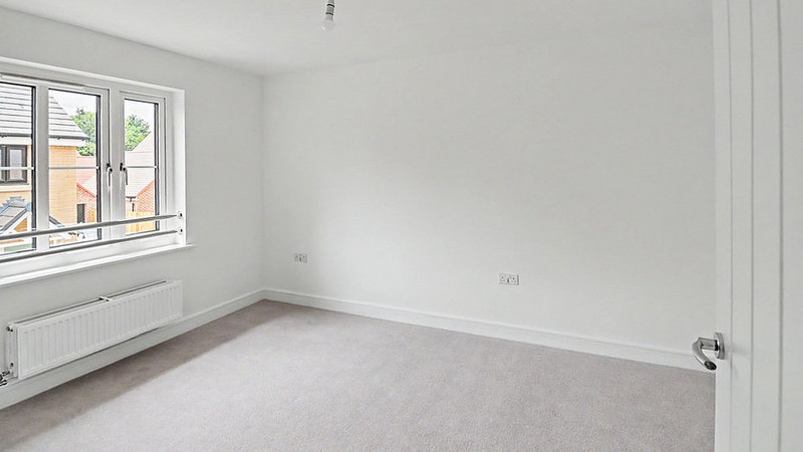 A bedroom with a window, radiator, and a door.
