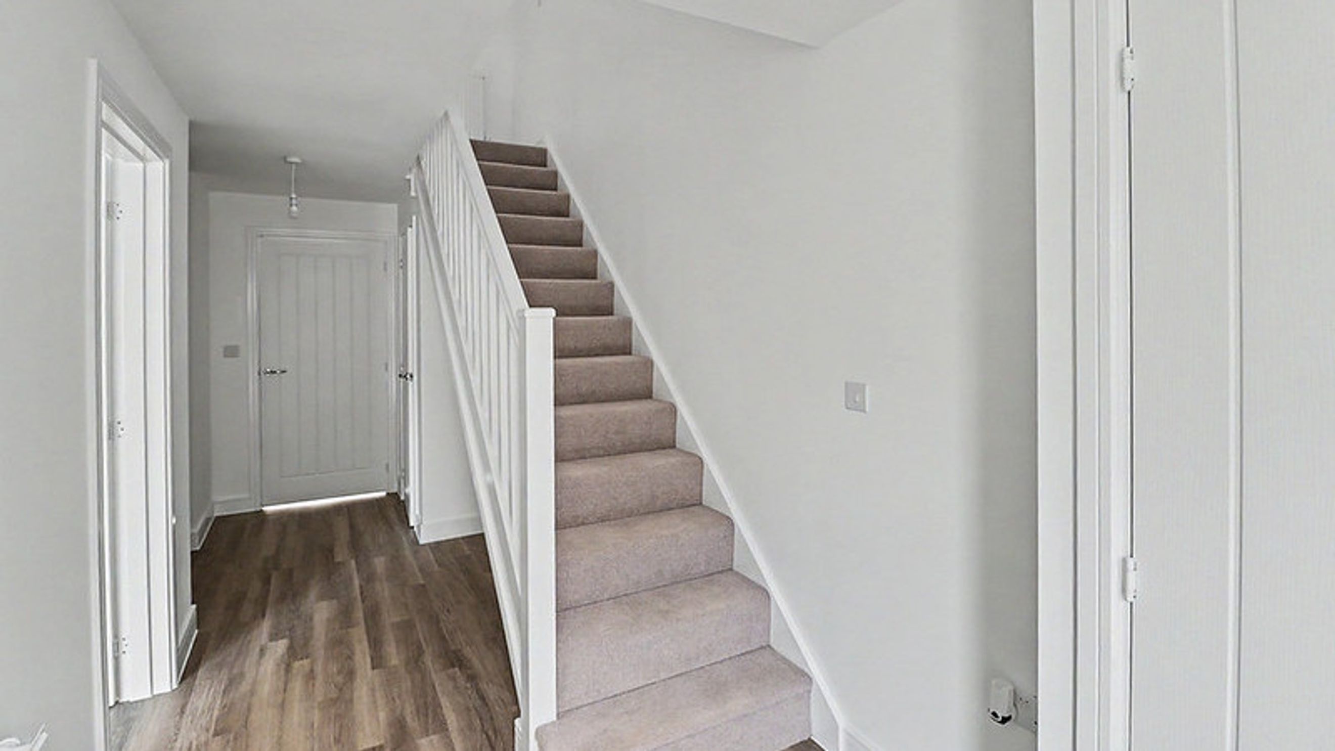 A hallway with a staircase, doors, and wood-effect flooring.
