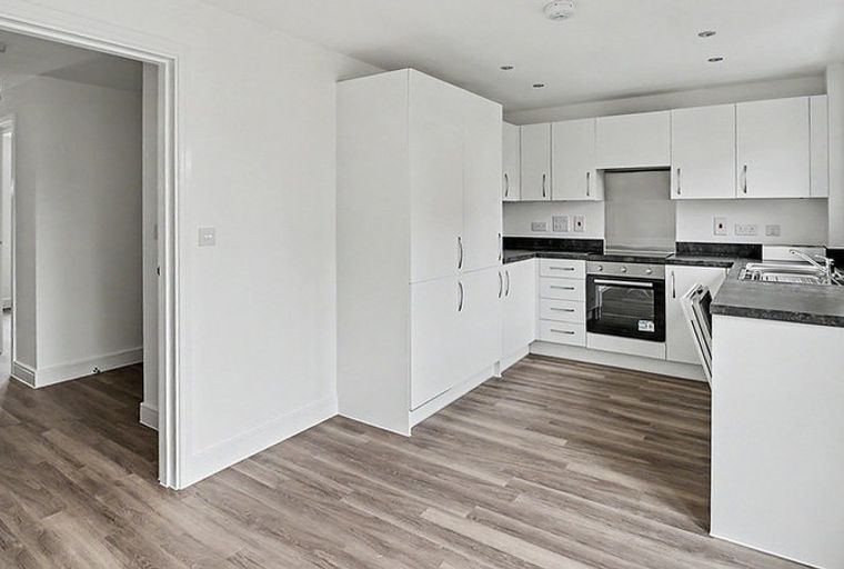 A modern kitchen with white cabinets, a dark countertop, and a built-in oven, adjacent to a hallway.