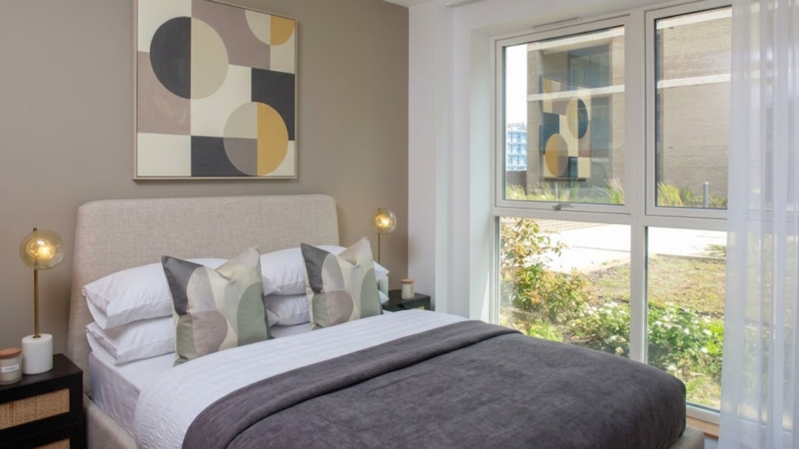 A bedroom with a bed, pillows, a blanket, a bedside table, a lamp, and a painting on the wall.