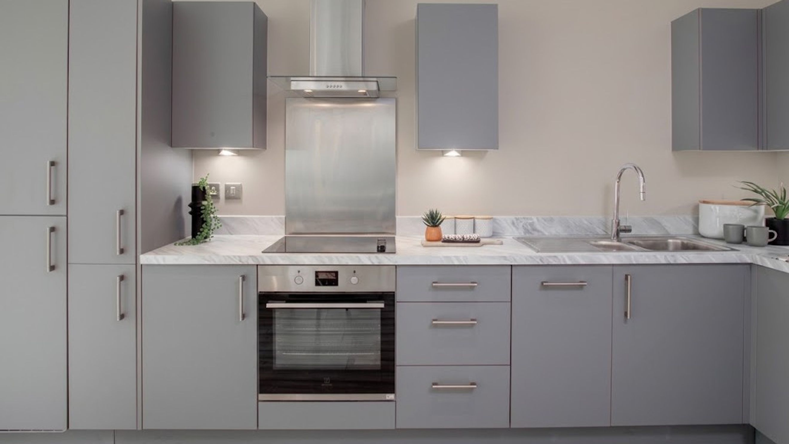 A modern kitchen with grey cabinets, a marble-effect countertop, and stainless steel appliances.