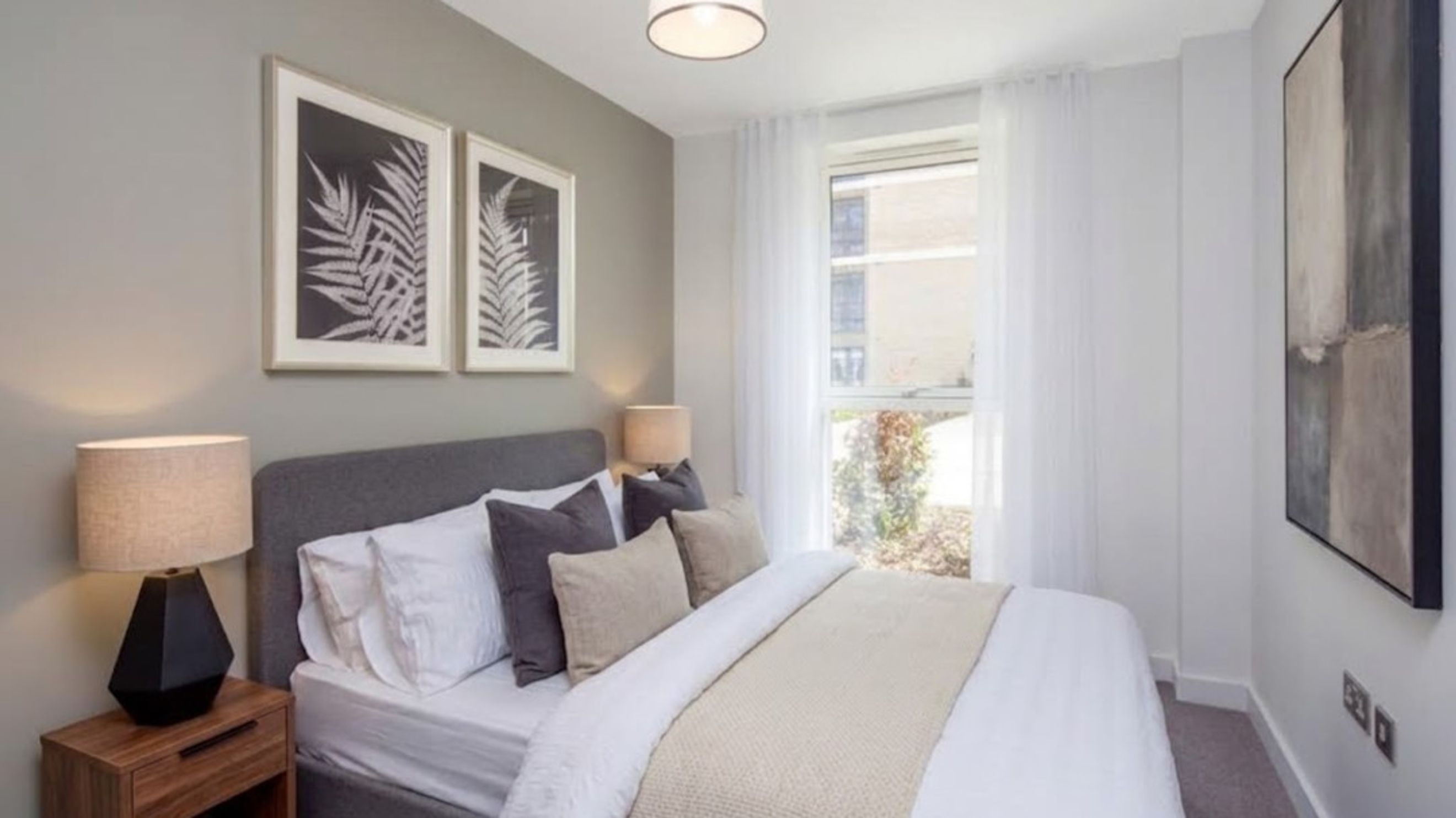 A bedroom with a bed, pillows, a bedside lamp, and framed artwork.