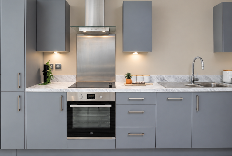 A modern kitchen with grey cabinets, a built-in oven, a stovetop, and a double sink.