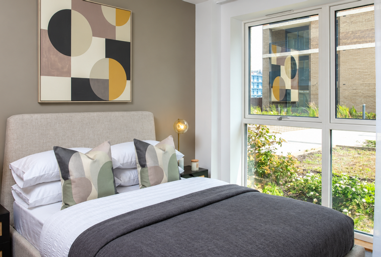 A bedroom with a bed, pillows, a bedside table, a lamp, and a painting on the wall.
