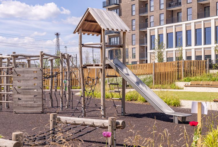 A children's playground with a slide and climbing structures next to a modern apartment building.