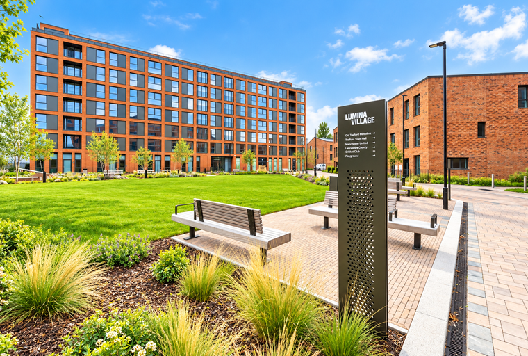 A modern apartment building with a manicured lawn and benches in front of a directional sign.