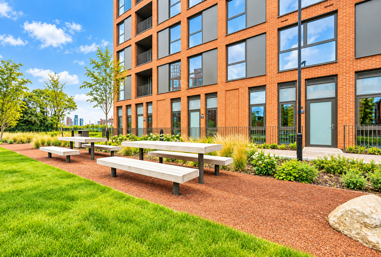 A modern apartment building with a landscaped courtyard featuring picnic tables.