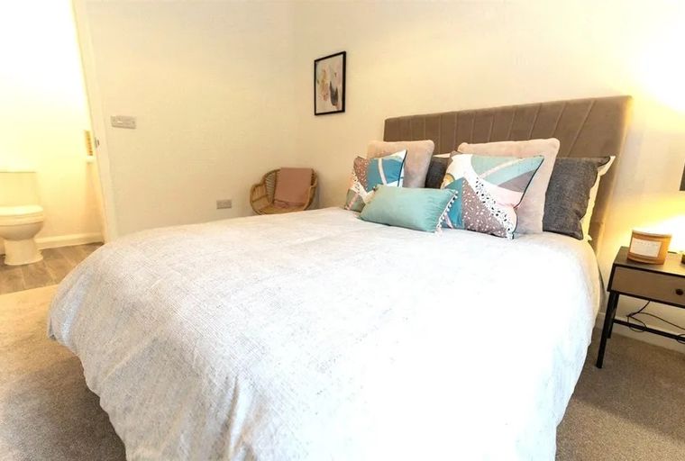 A bedroom with a bed, pillows, a chair, and an ensuite bathroom with a toilet.