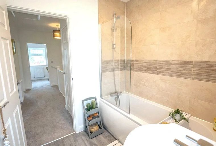 A bathroom with a bathtub and shower screen, adjacent to a carpeted hallway.