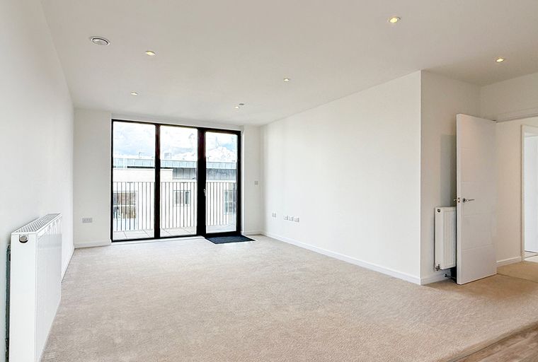 A living room with carpet, radiators, and large glass doors leading to a balcony.