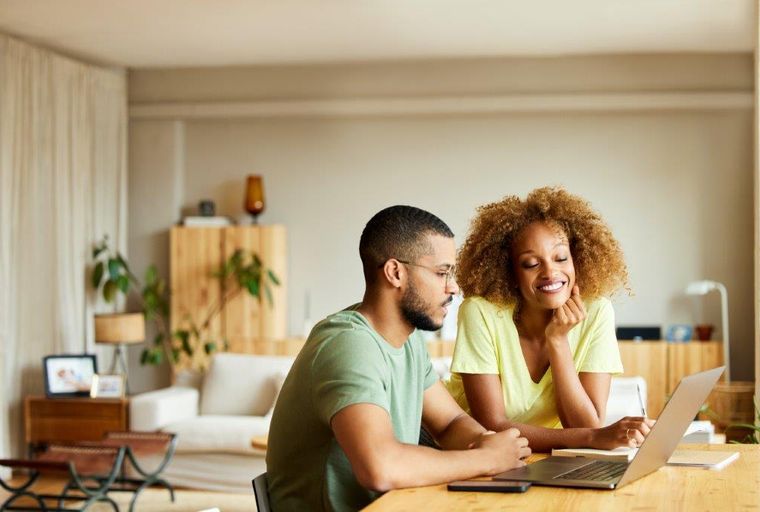 A man and a woman looking at a laptop on a table in a room.