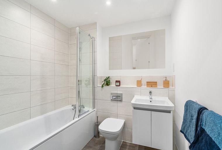 A bathroom with a bathtub, shower screen, toilet, sink, and mirror.