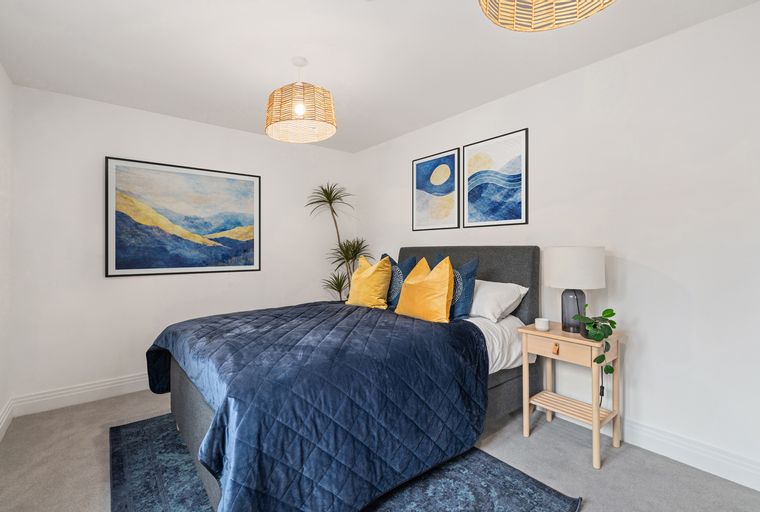 A bedroom with a bed, pillows, nightstand, lamp, and artwork.