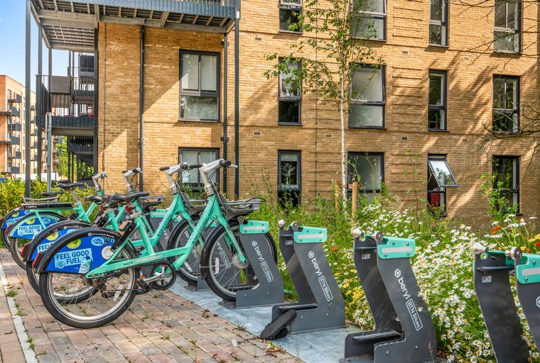 A row of teal Beryl bikes parked in front of a brick building with balconies and windows.