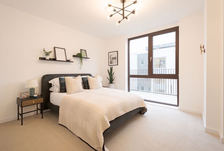 A bedroom with a bed, bedside table, lamp, and a large window.