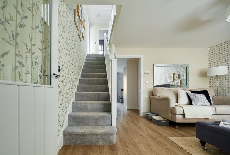 A hallway with a carpeted staircase and a living room with a sofa and ottoman.