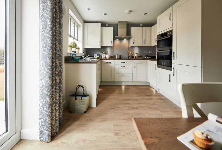 A modern kitchen with cream cabinets, stainless steel appliances, and a window.