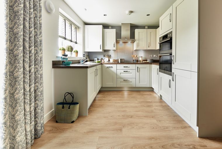 A modern kitchen with white cabinets, stainless steel appliances, and a wooden floor.