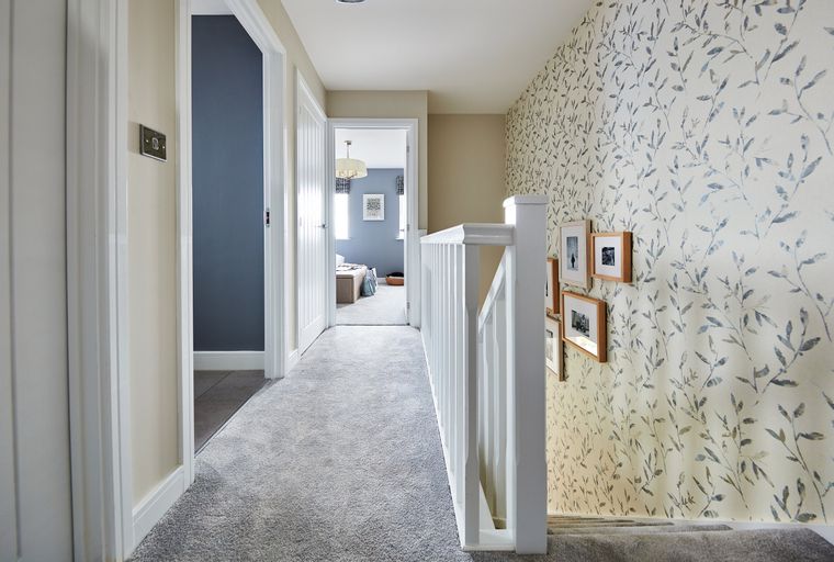 A hallway with doors, a carpeted floor, and a staircase with a white banister.