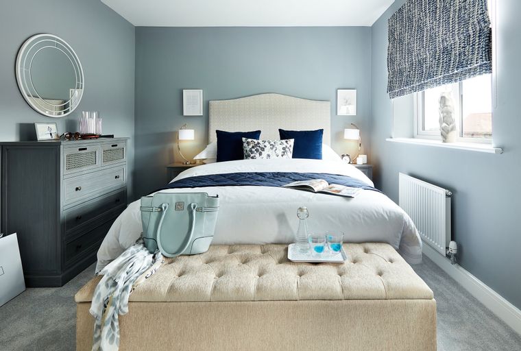 A bedroom with a bed, dresser, and ottoman.