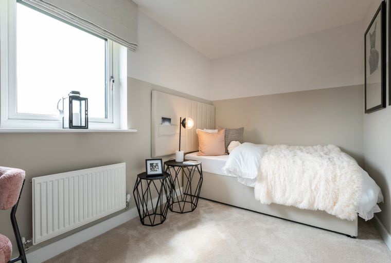 A bedroom with a bed, pillows, a lamp, and a window.