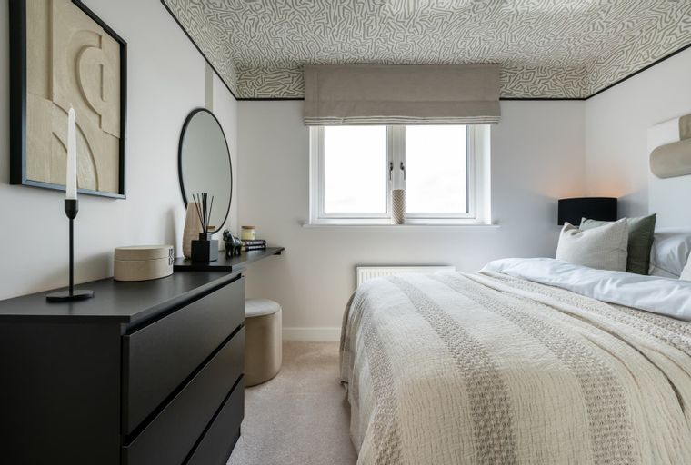 A bedroom with a dresser, a mirror, a bed, and a window.