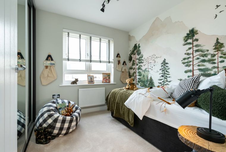 A child's bedroom with a forest mural, bed, beanbag chair, and window.