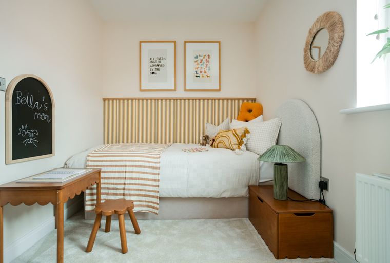 A child's bedroom with a bed, desk, stool, and chalkboard.