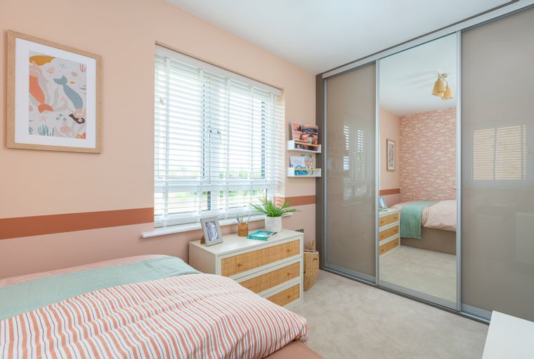 A bedroom with a bed, dresser, and a large mirrored wardrobe.